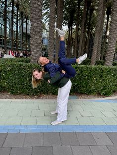 a man and woman doing an acrobatic pose on the sidewalk in front of palm trees