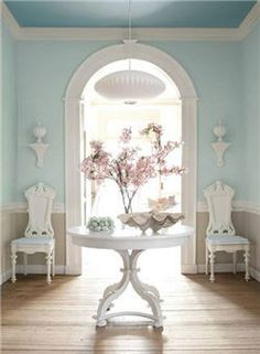 a white table and chairs in front of a window with pink flowers on the table