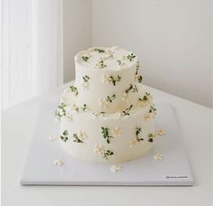 a three tiered cake with white flowers and green leaves on the top is sitting on a plate