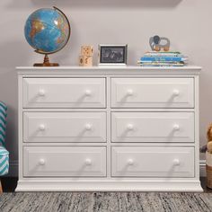 a white dresser sitting in a bedroom next to a blue chair and a globe on top of it