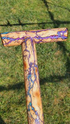 a wooden walking stick with purple and blue paint on it in the middle of grass