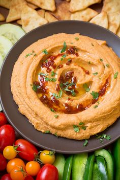 a black plate topped with hummus, tomatoes and cucumbers next to crackers