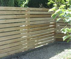 a wooden fence in the middle of a graveled area next to some bushes and trees