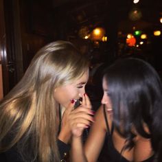 two beautiful young women standing next to each other in front of a mirror talking on their cell phones