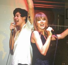 two people singing into microphones in front of a tv screen with one person raising his arm