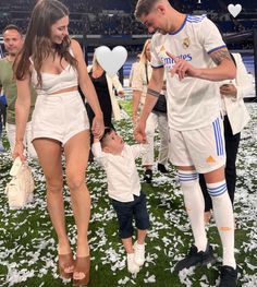 a man and woman holding hands with a small child in front of them at a soccer game