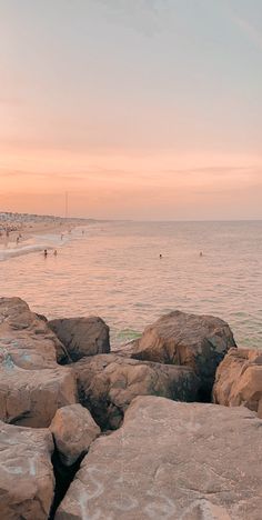 people are swimming in the water at sunset on rocks near the beach with surfboards