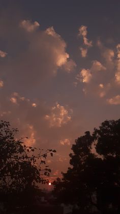 the sun is setting behind some trees on a cloudy day with clouds in the sky