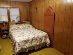 a bed in a room with wooden paneling on the walls and a dresser next to it