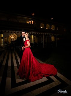 a man and woman in formal wear posing for a photo at night with their arms around each other