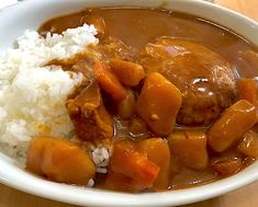 a white bowl filled with rice and meat covered in gravy on top of a wooden table