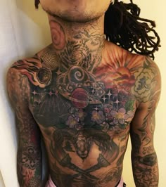 a man with lots of tattoos on his chest and back, standing in front of a white wall