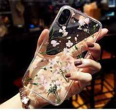 a woman's hand holding up a clear case with white flowers on it and greenery