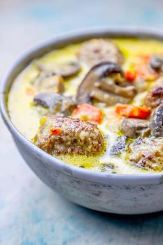 a bowl filled with meatballs and vegetables on top of a blue countertop next to a spoon