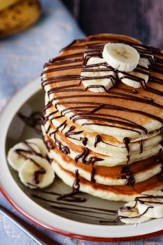 a stack of pancakes topped with banana slices and chocolate drizzled on top