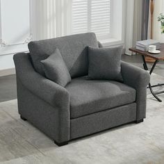 a gray chair sitting on top of a rug in a living room next to a window