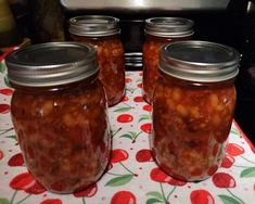 four jars filled with food sitting on top of a red and green tablecloth covered table