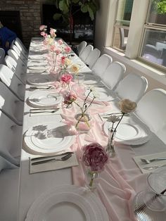 the long table is set with white plates and pink flowers in vases on it