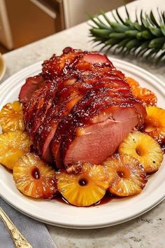 a white plate topped with meat covered in sauce next to sliced pineapples and orange slices