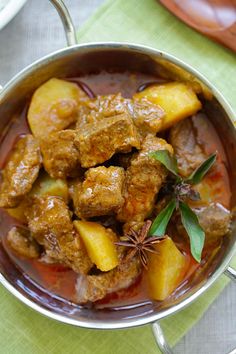 meat and pineapple stew in a metal bowl on a green tablecloth with spoons