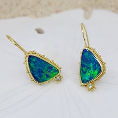 Escape into the beauty of the sea with these stunning Opal & Diamond Earrings. Crafted from 18K granulated gold and adorned with gorgeous blue-green opals and two small diamonds, these earrings shimmering like the rolling waves of a distant shore. Treat yourself to a little oasis with these charming ocean-inspired earrings 18KY granulated earrings with 2 opal doublets weighing 8.42cts and accented with .06cttw of VS/GH diamonds.Dimensions: 7/8” x 9/16” (24mm x 15mm) excluding earwire Yellow Gold Opal Gemstone Earrings, Ocean Inspired Earrings, Ocean Inspired, Green Opal, Ocean Inspiration, Stone Settings, Jewelry Inspiration, The Sea, Oasis