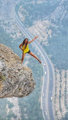 a woman standing on top of a cliff next to a road