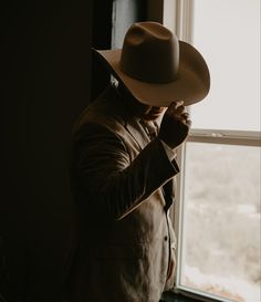 a man in a suit and hat standing next to a window looking out the window