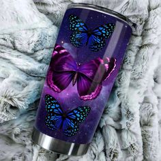 a purple and blue butterfly travel mug sitting on a white fur covered blanket with the lid open