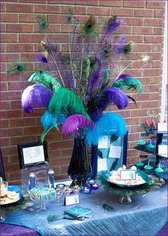 a table topped with plates and vases filled with purple, green and blue feathers