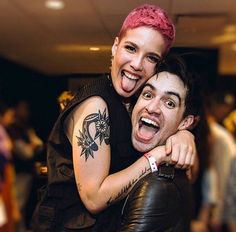 two people are hugging each other in a room full of people and one person has pink hair