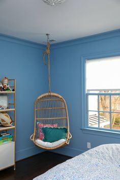 a bedroom with blue walls and a hanging swing chair in the middle of the room