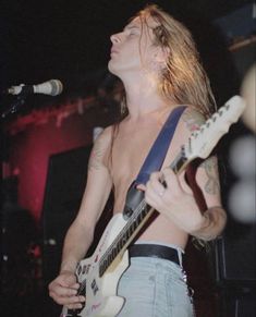 a man with long hair playing an electric guitar in front of a microphone on stage