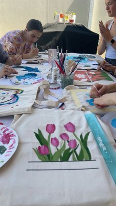 people sitting at a table with paper plates and flowers on it, while one woman is painting