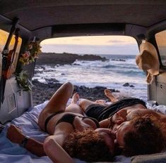 two people laying in the back of a truck on top of a bed next to the ocean