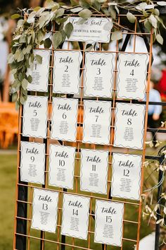 the seating cards were placed on an orange metal stand with greenery and foliage around them