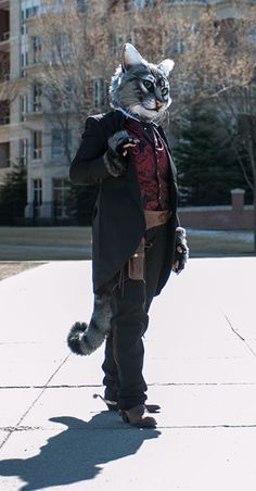 a man dressed up as a cat standing on the sidewalk in front of a building