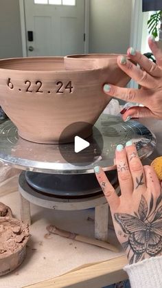 two hands are working on a clay bowl that is sitting on top of a table