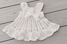 a white crocheted dress with a bow on the front and back, sitting on a wooden surface