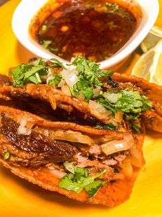 a yellow plate topped with meat and vegetables next to a bowl of dipping sauce on the side