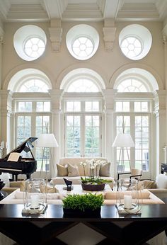 a living room filled with lots of furniture next to two large windows and a grand piano