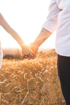 a man and woman holding hands in the middle of a wheat field with the sun behind them