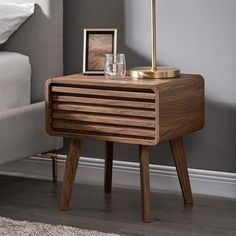 a night stand with two glasses on it next to a bed and a framed photograph