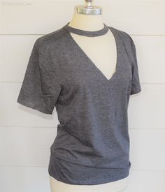 a mannequin wearing a gray shirt and black pants with a white wall in the background