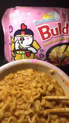 a bowl of noodles with chopsticks next to a bag of budda noodles