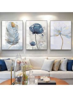 three paintings hanging on the wall above a white couch in a living room with blue accents