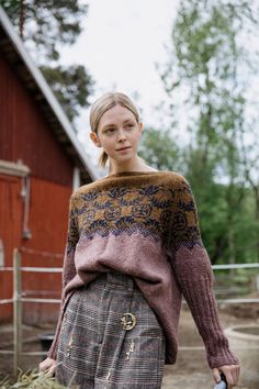 a woman standing in front of a red barn holding a blue frisbee and wearing a sweater