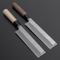 two knives are next to each other on a black surface, one has a wooden handle