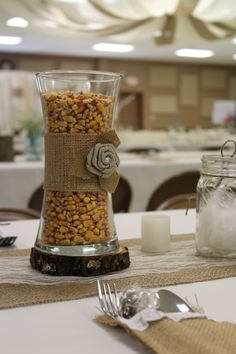 a glass vase filled with corn sitting on top of a table next to a fork