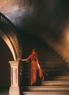 a woman in a red dress is standing on the stairs with her hand on the railing