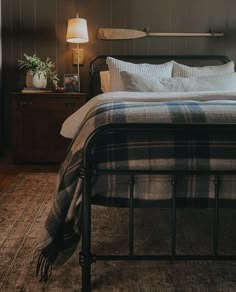 a bed with a plaid blanket and pillows on top of it next to a lamp